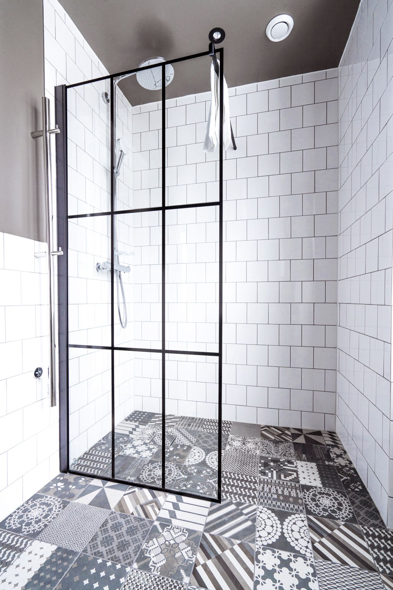 A shower area with a glass door, white tiled walls, and a patterned floor.