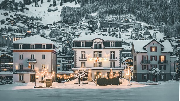 Un hôtel enneigé, avec plusieurs étages, des balcons et une entrée illuminée.