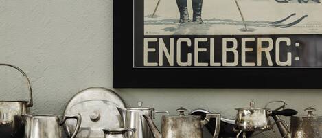 A collection of silver kitchenware on a shelf, including a kettle, teapot, and a large pot, with a framed picture of a skier above them.