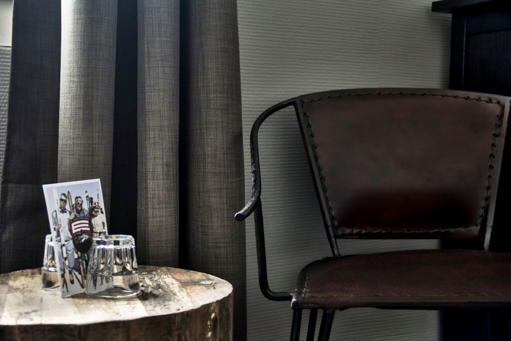 Une table en bois avec un verre et un cadre photo, une chaise en cuir et un rideau en arrière-plan.