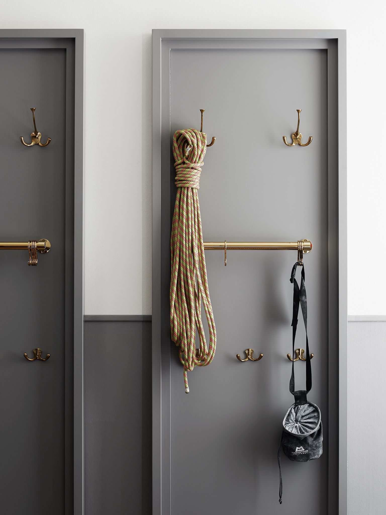 Une pièce avec une porte grise, une poignée de porte en laiton et une barre à serviettes en laiton sur laquelle sont accrochés une serviette et un sac.