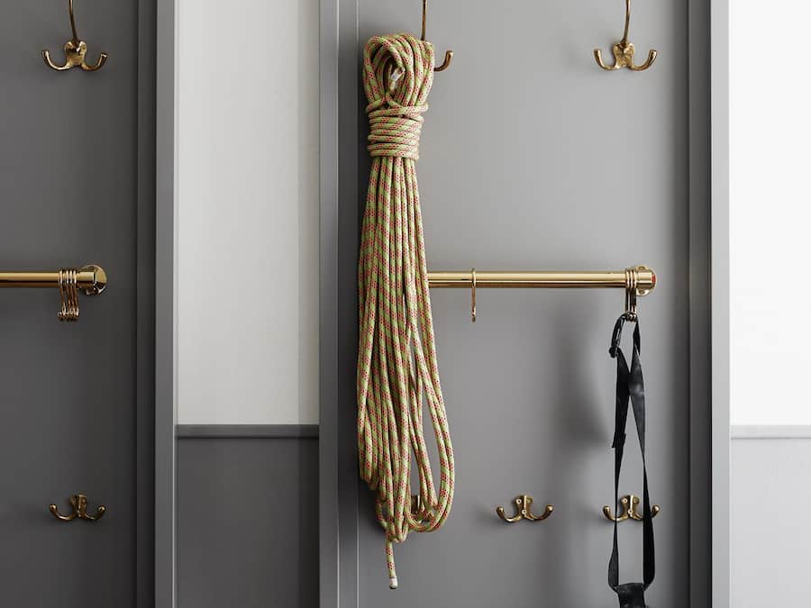 Une pièce avec une porte grise, une poignée de porte en laiton et une barre à serviettes en laiton sur laquelle sont accrochés une serviette et un sac.