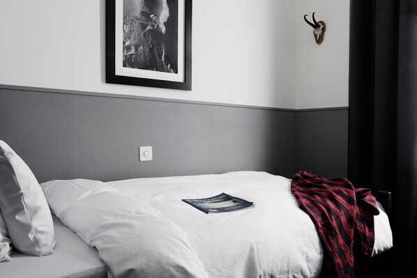 A neatly made bed with white linens, a magazine on the bed, a red and black blanket, a framed picture on the wall, and a mounted animal head.