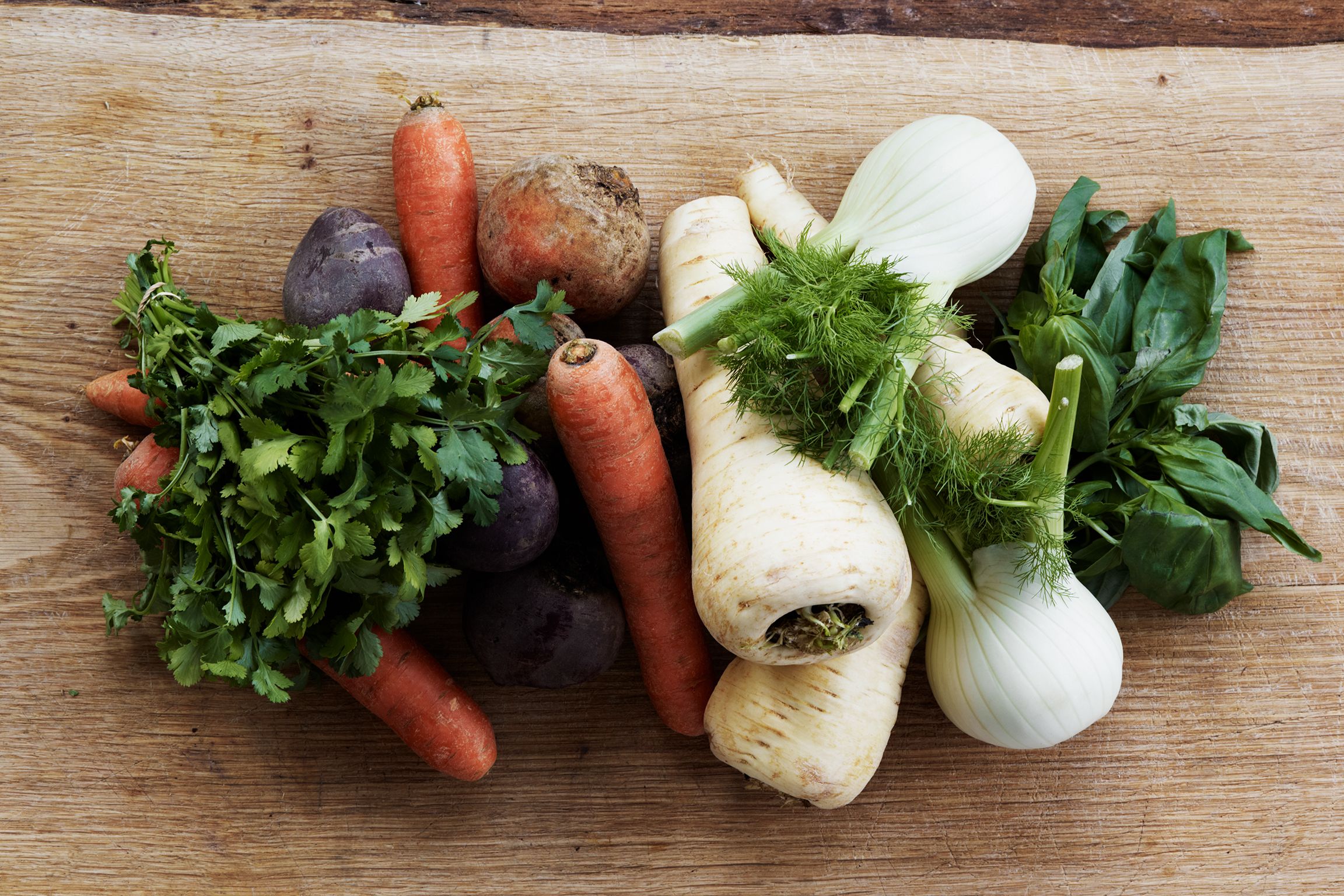 A variety of vegetables including carrots, beets, and onions on a wooden surface.