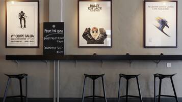 A wall with three framed posters, a blackboard with handwritten notes, and three black stools.