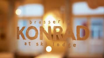 Vista borrosa del interior de un restaurante con el nombre "brasserie KONRAD at ski lodge" visible en una superficie de vidrio.