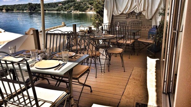 An outdoor dining area with tables and chairs, overlooking a body of water and a hillside. - Six Keys Seaside Lodge (South Pelion)