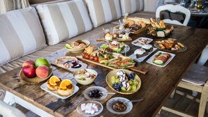 A wooden dining table with various food items and a bowl of fruit. - Six Keys Seaside Lodge (South Pelion)