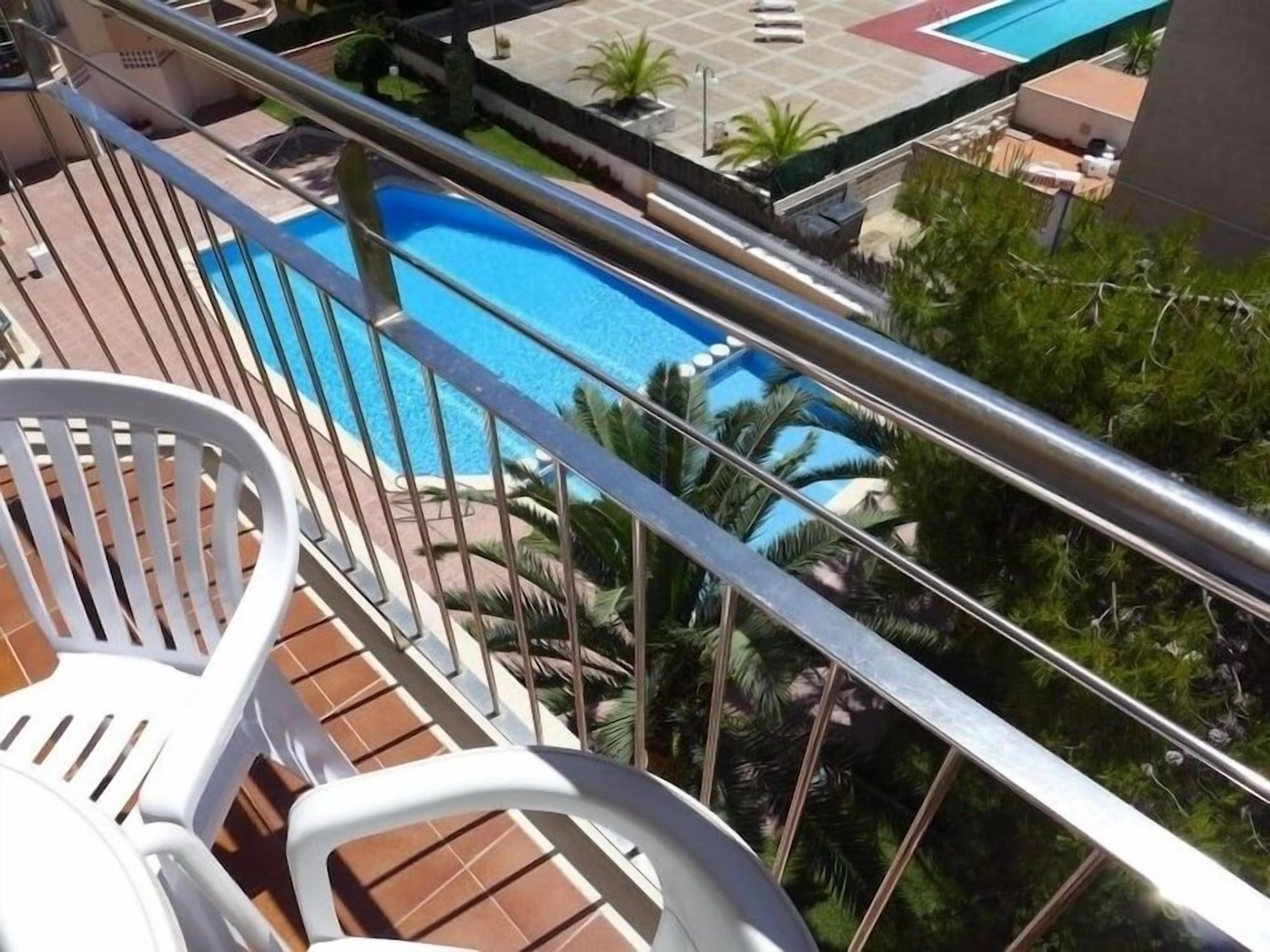Ein Poolbereich mit freiem Blick auf das Wasser, umgeben von Palmen und einer gefliesten Terrasse.