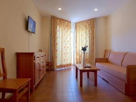 Una sala de estar con un sofá, una mesa de centro, un televisor montado en la pared y un mueble.