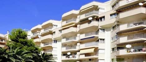 A multi-story hotel with balconies, a swimming pool, and palm trees.