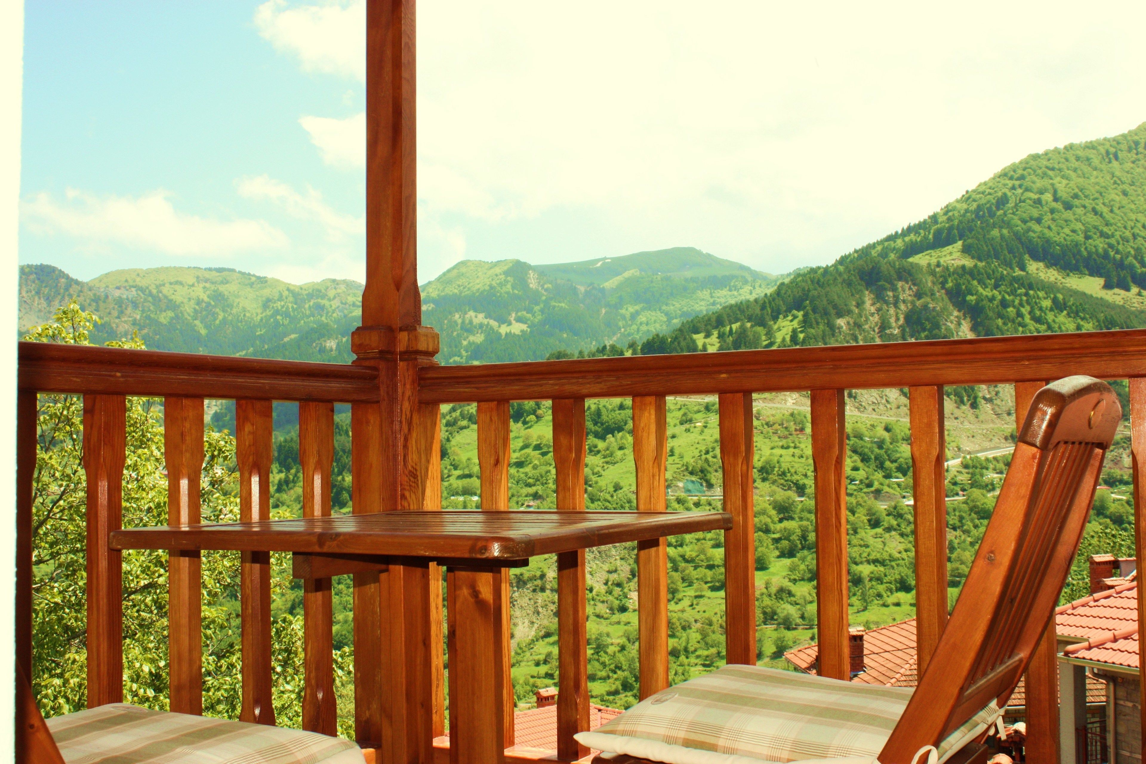 Terraza de madera con dos sillones acolchados a rayas y una pequeña mesa, con vistas a un paisaje montañoso.