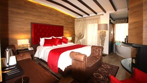 A hotel room with a large bed, a wooden headboard, a desk with a chair, a coffee maker, and a nightstand with a lamp. - Archontiko Metsovou Boutique Hotel (Metsovo)