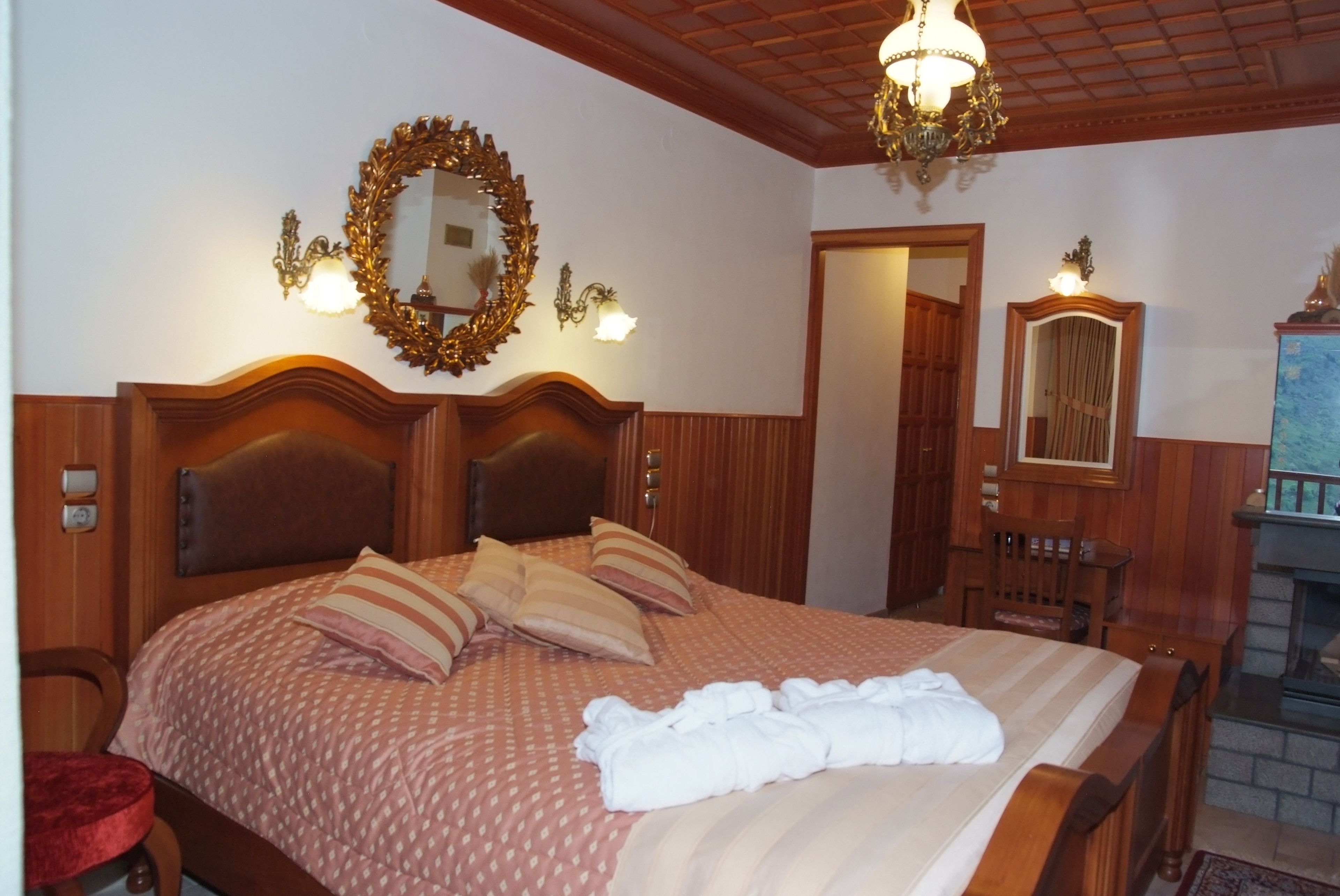 Una habitació d'hotel amb un llit gran, un panell frontal de fusta, un mirall i una llar de foc.