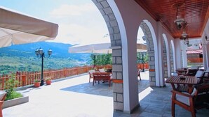 A covered outdoor area with stone pillars, wooden furniture, and a view of a mountainous landscape. - Archontiko Metsovou Boutique Hotel (Metsovo)