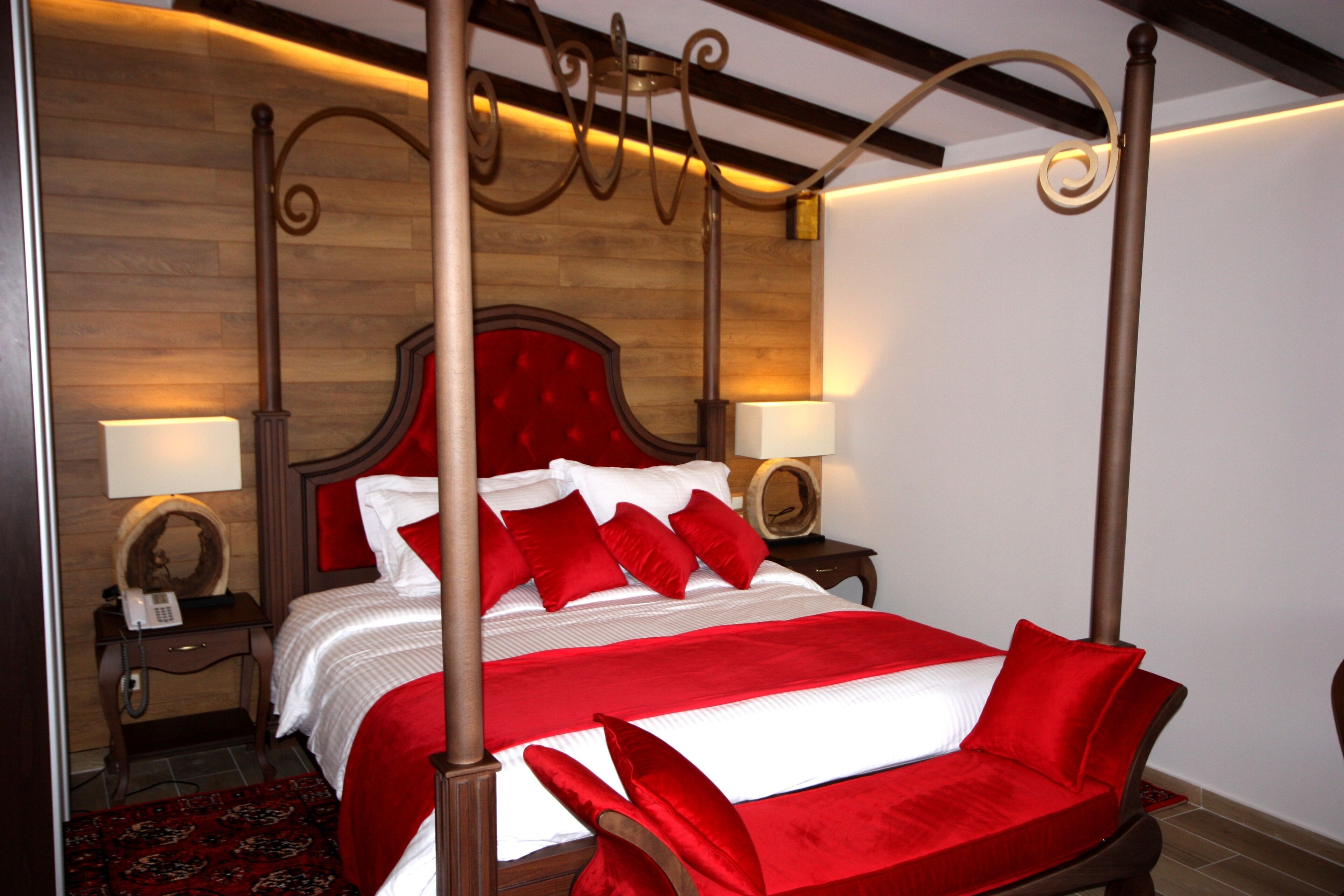 A four-poster bed with a red and white bedspread, two bedside tables with lamps, and a wooden headboard.