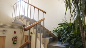 Una escalera con barandillas de madera y escalones de piedra, un extintor y plantas en macetas.