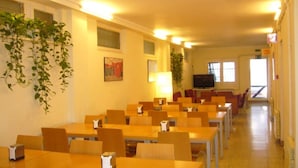 Un comedor con varias mesas y sillas, un televisor y plantas en macetas.
