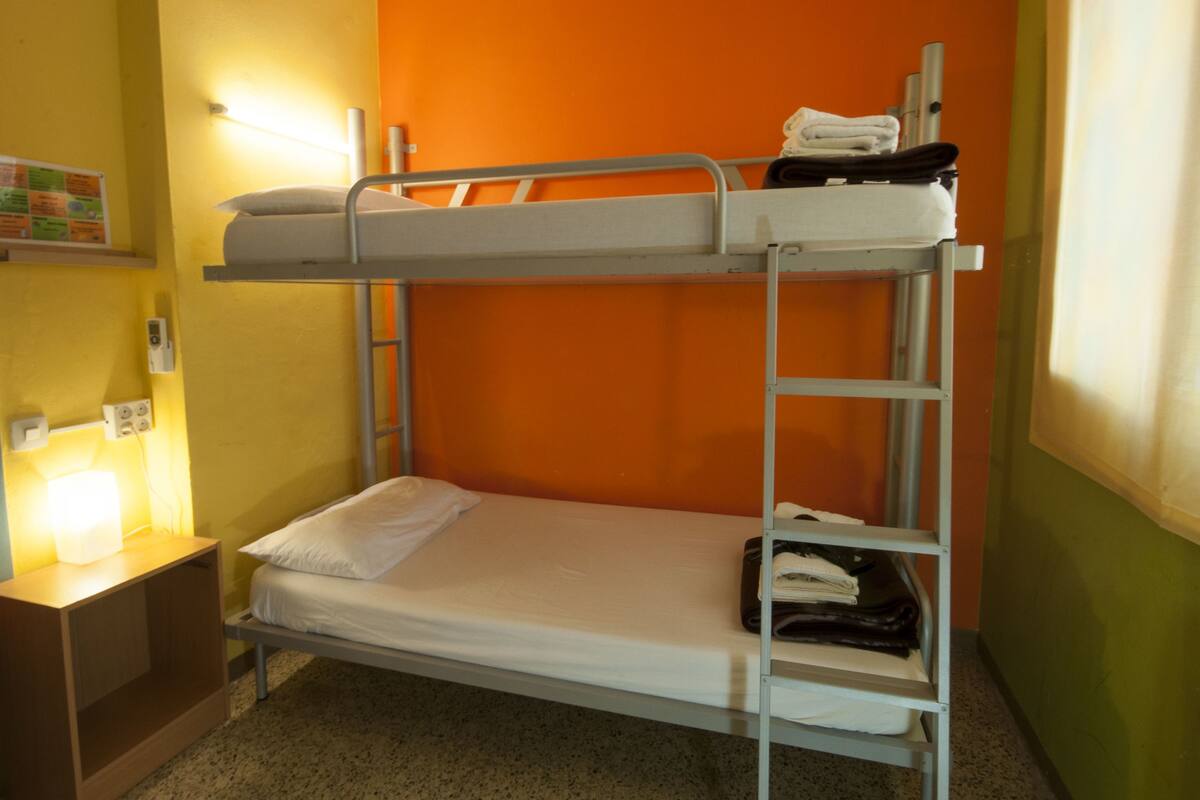 A bunk bed room with a nightstand, a lamp, and a folded towel on the top bunk.