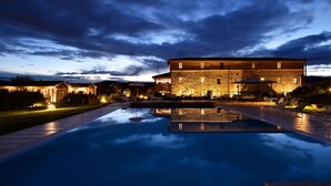 A large stone building with a pool in front, surrounded by well-lit outdoor seating areas. - Anna Boccali Resort (Corciano)
