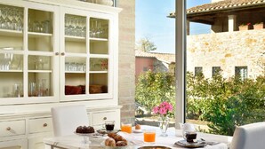 A breakfast table with pastries, coffee, and juice, set against a stone building with a garden view. - Anna Boccali Resort (Corciano)