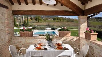 Une terrasse extérieure avec une table dressée pour le repas, offrant une vue sur une piscine et un paysage pittoresque.