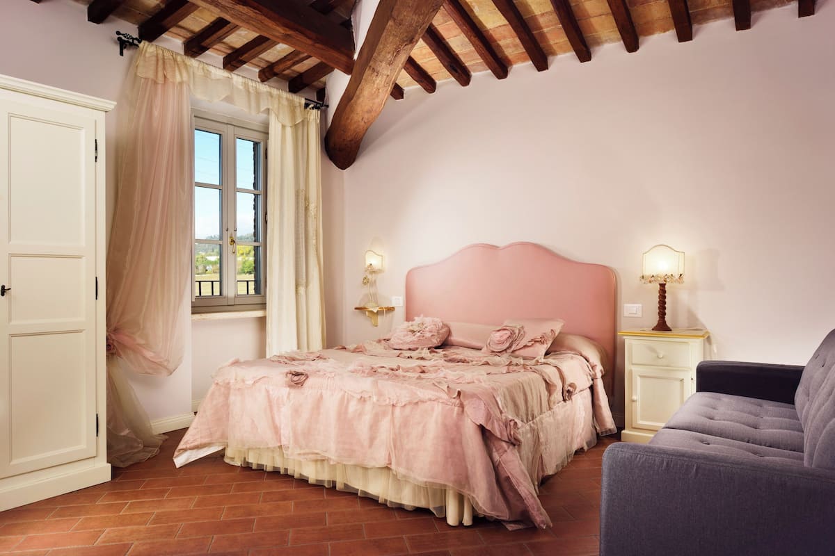 A bedroom with a bed, a chair, a nightstand, and a window with curtains.