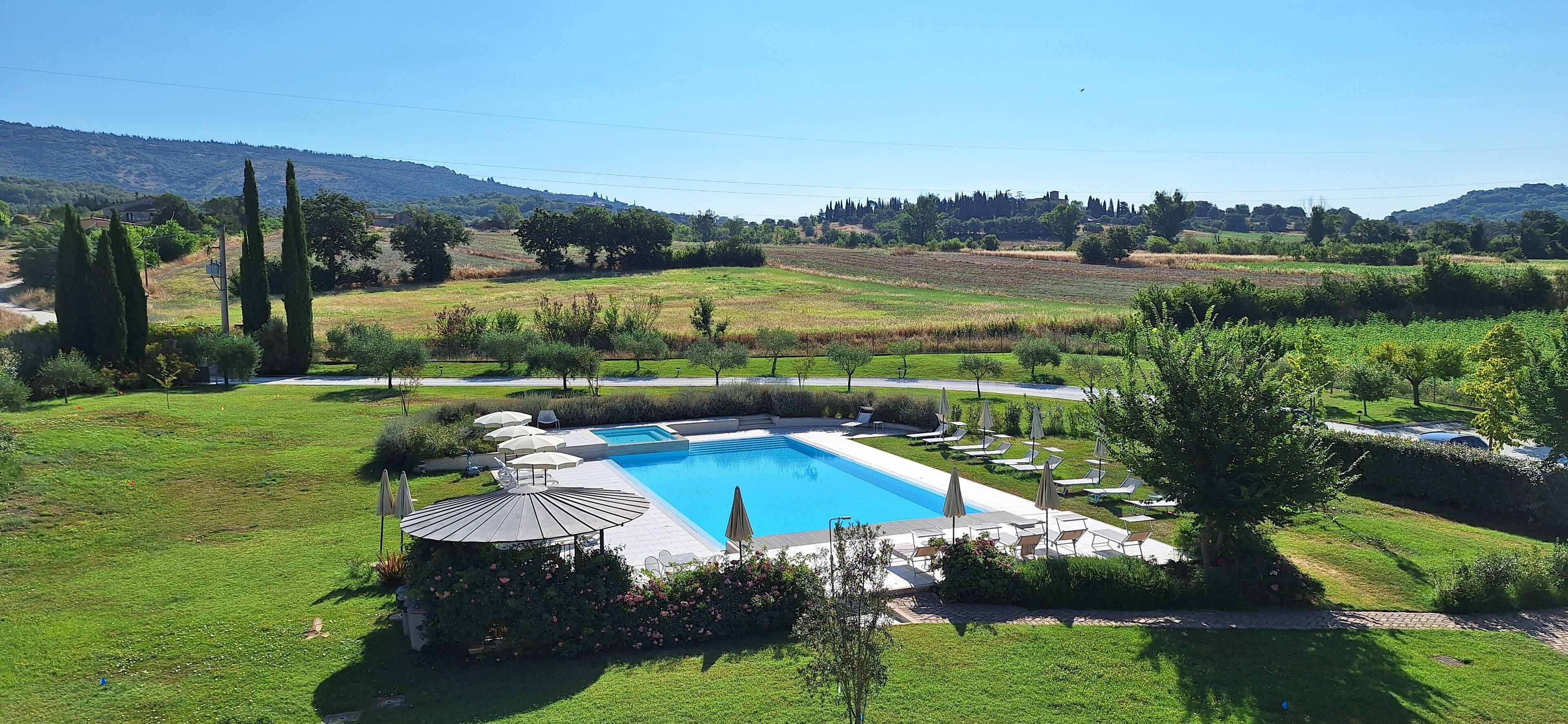 Piscina con sillones de descanso y sombrillas, rodeada de césped cuidado y árboles.
