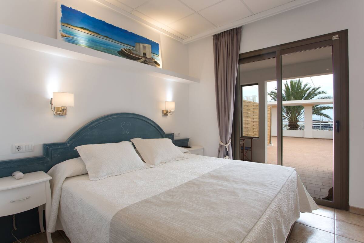 Ein Hotelzimmer mit Bett, Nachttischen, einem Gemälde und Blick ins Freie.