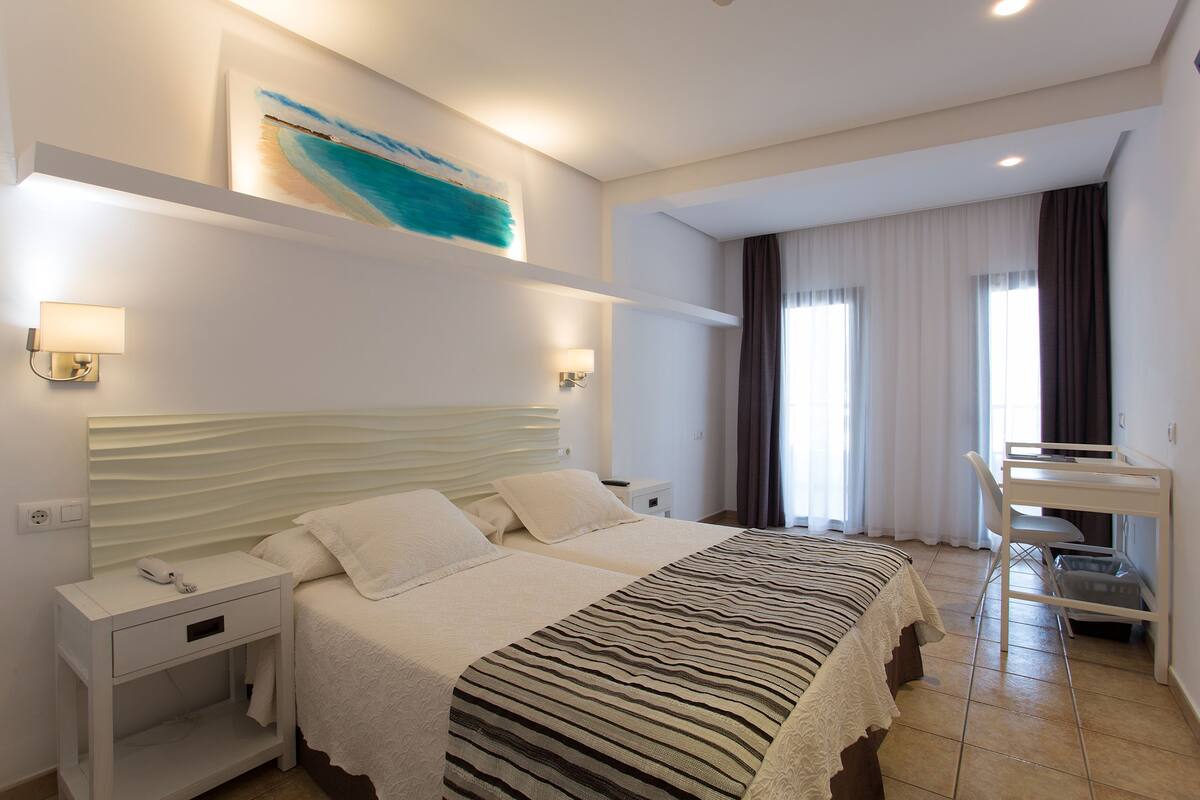 Ein Hotelzimmer mit einem großen Bett, Nachttischen, einem Schreibtisch und einem Sessel.