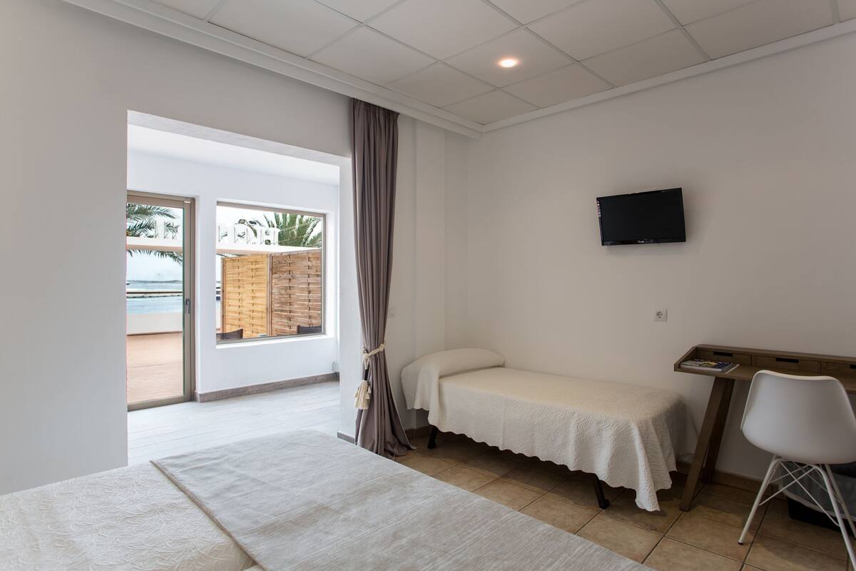 Ein Schlafzimmer mit Bett, Schreibtisch, Sessel, Fernseher und Blick ins Freie.