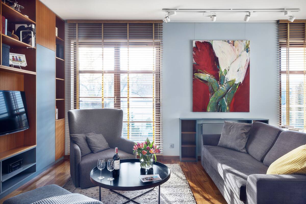 Ein modernes Wohnzimmer mit einem grauen Sofa, einem Couchtisch mit Blumenvase, einem Flachbildfernseher und einem Bücherregal.