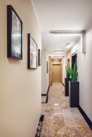 A hotel hallway with framed pictures on the walls, a door labeled "12", and potted plants. - Jovi Apartments (Sopot)