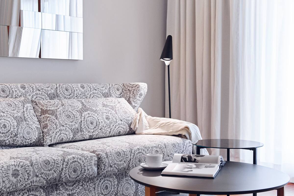 Ein modernes Wohnzimmer mit einem gemusterten Sofa, einem runden Couchtisch und einem schwarzen Hocker.