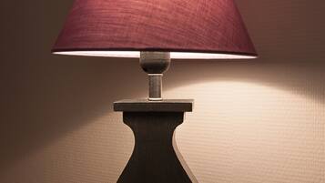 A table lamp with a dark base and a red shade, placed on a white surface against a textured wall.