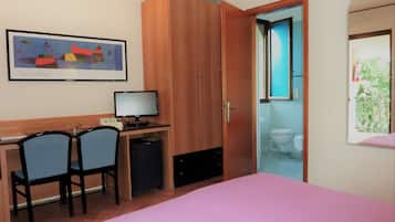 Une chambre à coucher comprenant un lit, un bureau avec deux chaises, un ordinateur et une porte donnant sur une salle de bain.