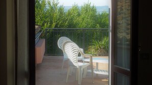 A balcony with a white plastic chair, a potted plant, and a view of greenery and distant hills. - Hotel La Rocca (Narni)