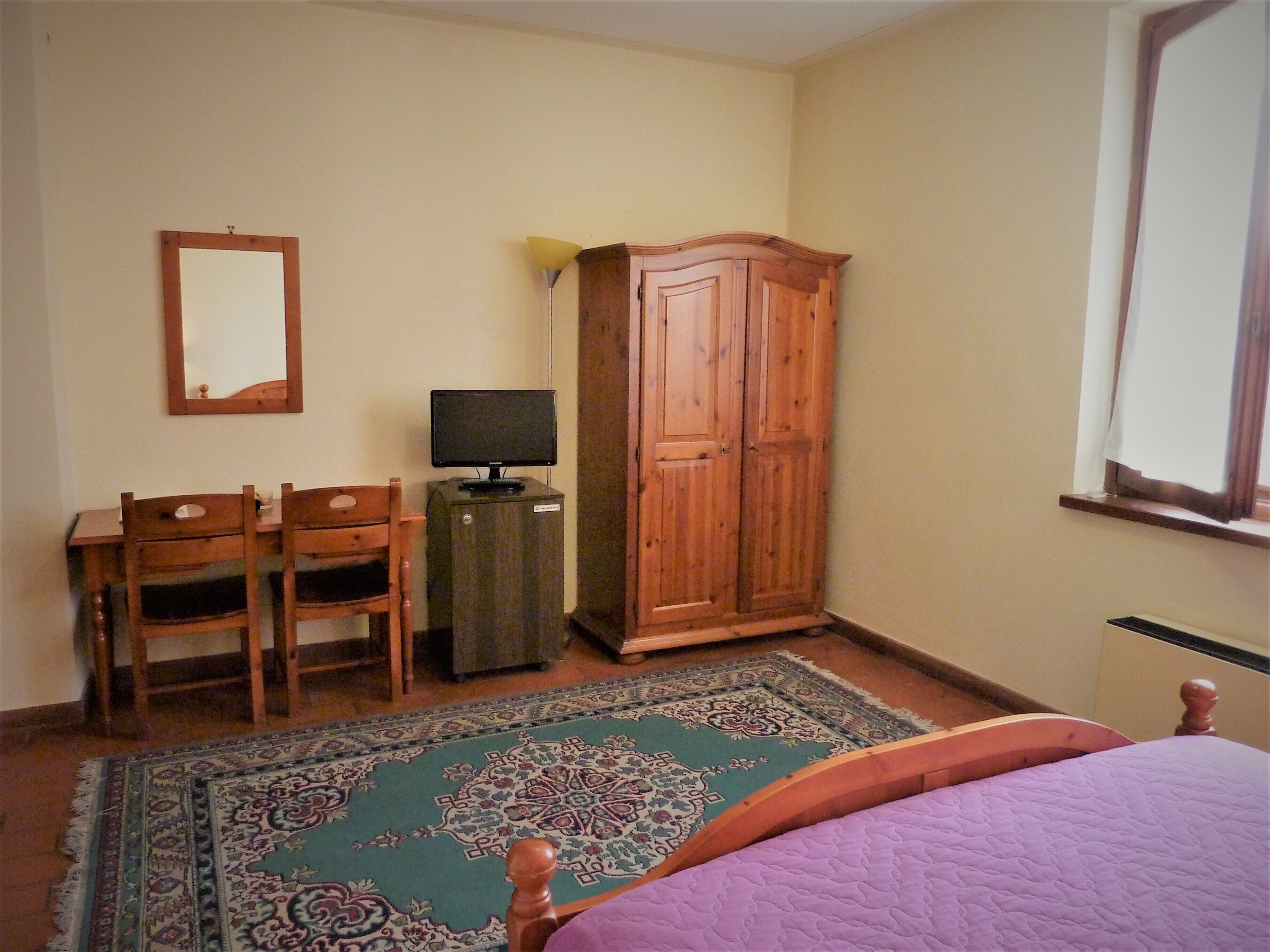 A bedroom with a bed, a desk with a computer, a wardrobe, and a mirror.