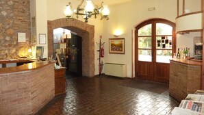 A lobby with a reception desk, a chandelier, a fireplace, and a door leading to another room. - Hotel La Rocca (Narni)