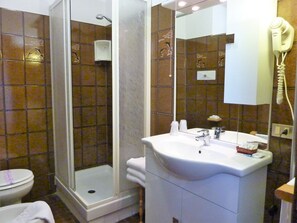 A bathroom with a glass shower enclosure, a sink with a mirror, and a hairdryer mounted on the wall.