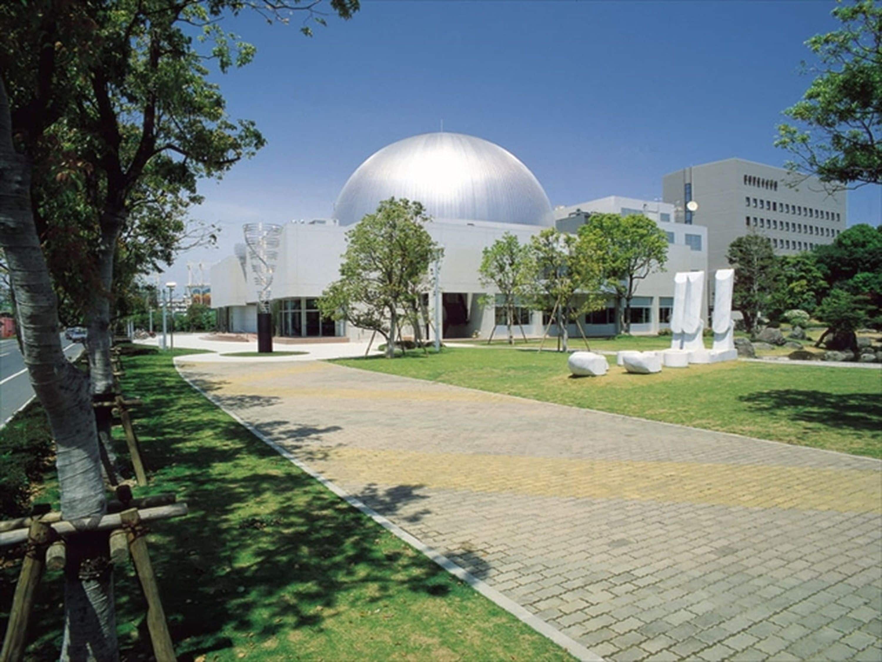 A modern building with a large dome structure, surrounded by a paved walkway and greenery.