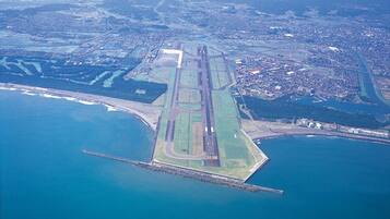 Vista aérea de un aeropuerto costero con una pista larga, una masa de agua adyacente y zonas urbanas circundantes.