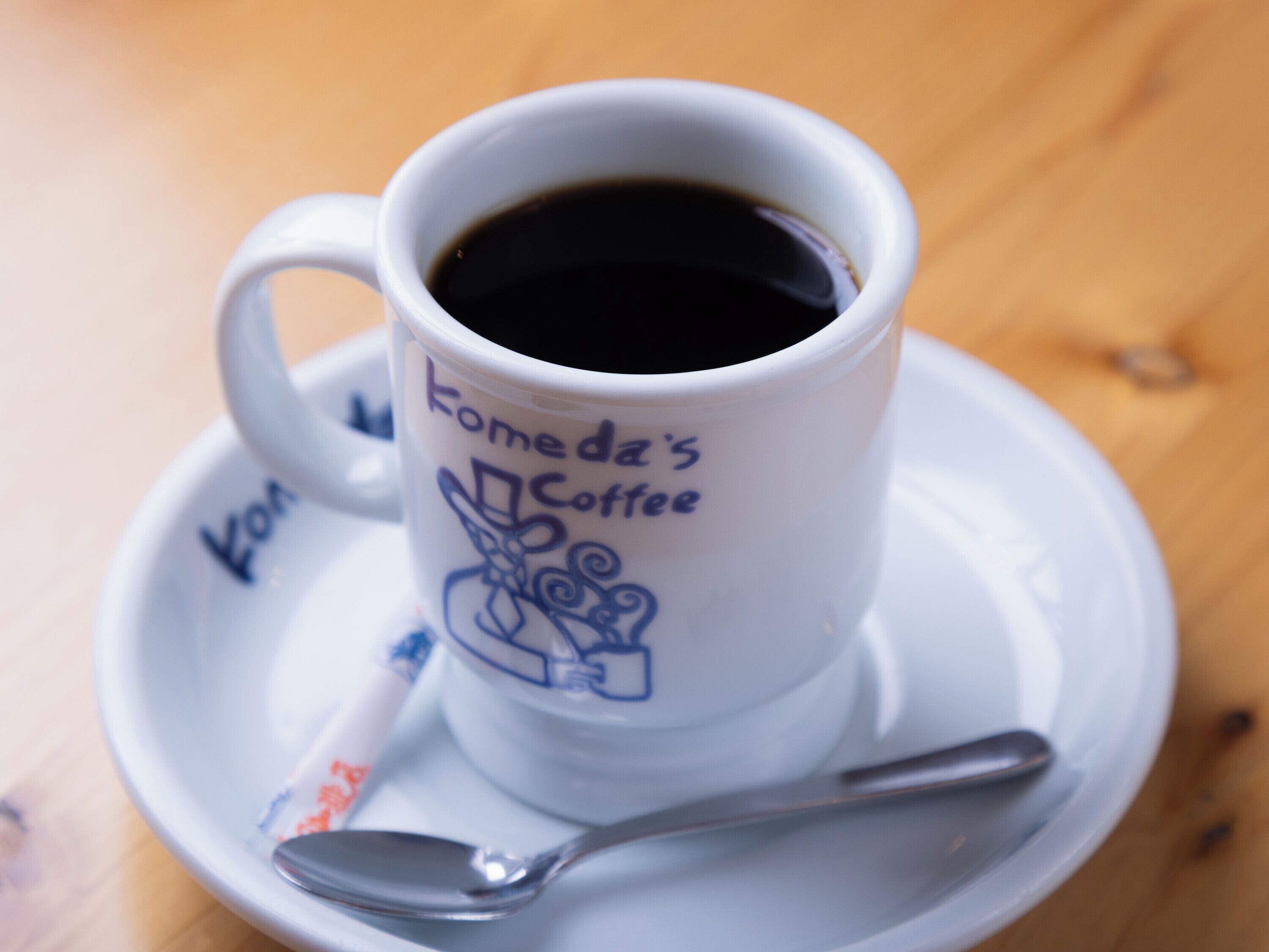 Uma chávena de café branca com uma colher num pires, com a inscrição 'Komeda's Coffee'.