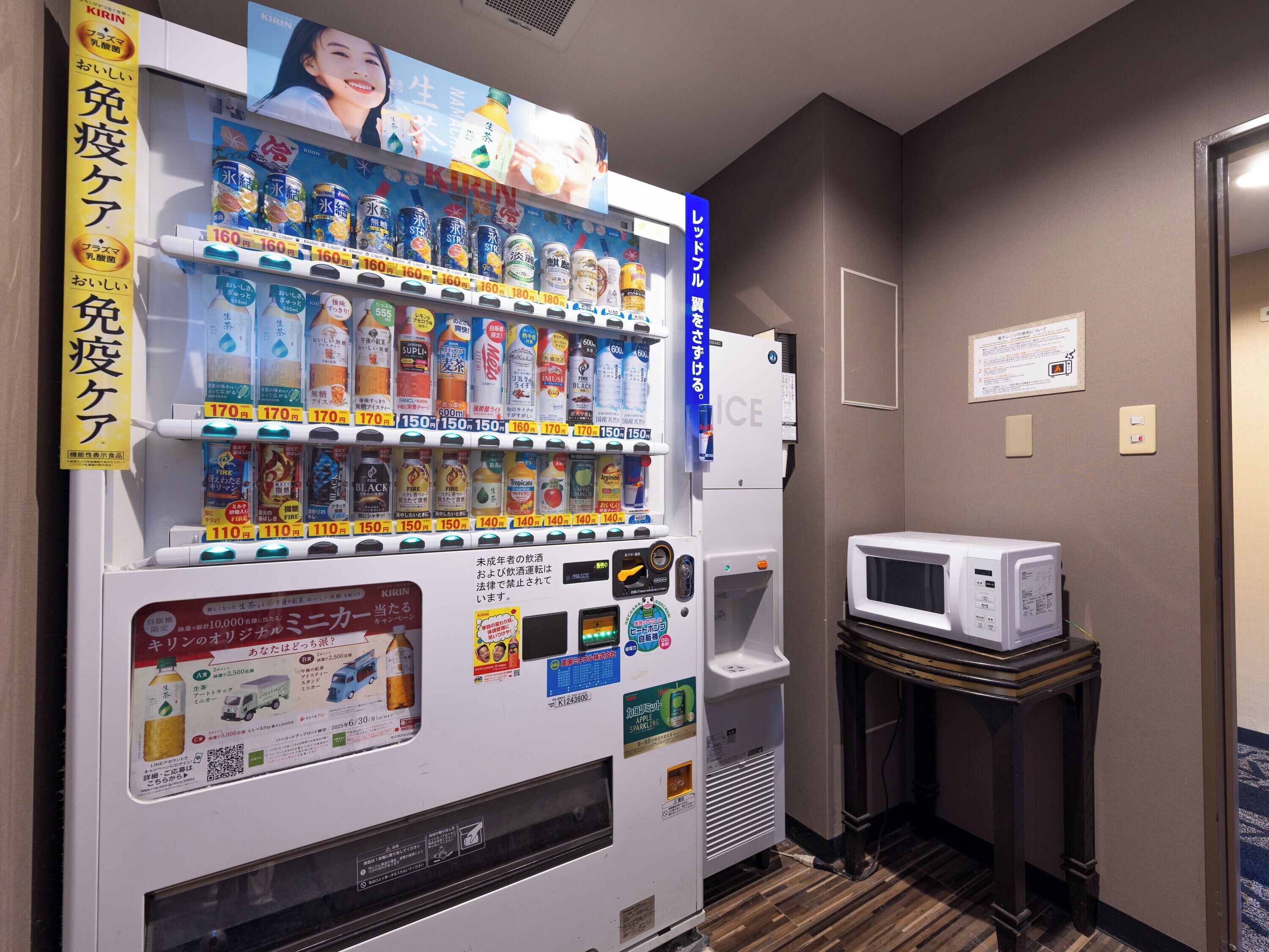 Een automaat gevuld met drankjes en snacks, een magnetron en een klein tafeltje met een afstandsbediening.