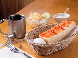 Una mesa con una taza de metal, un tazón de vegetales rallados, una cesta con pan y un huevo, y un recipiente pequeño con crema.