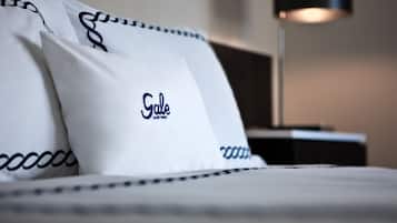 A neatly made bed with white bedding and black trim, featuring pillows with the text "Gale South Tech."