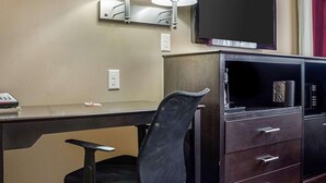 Une chambre d’hôtel équipée d’un bureau, de deux lampes fixées au mur, d’un téléviseur à écran plat, d’une chaise et d’un mini-bar.