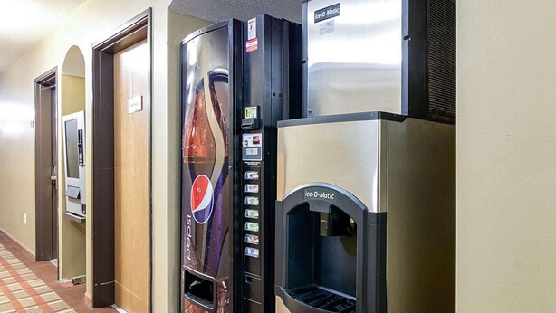 Un couloir d’hôtel avec un distributeur automatique, un réfrigérateur et une porte.