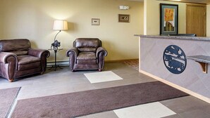 Un hall d’entrée avec deux fauteuils en cuir, un comptoir de réception avec une horloge et un tableau encadré au mur.