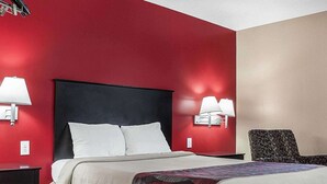 Une chambre d’hôtel avec un lit, deux lampes de chevet, une chaise et un mur rouge.